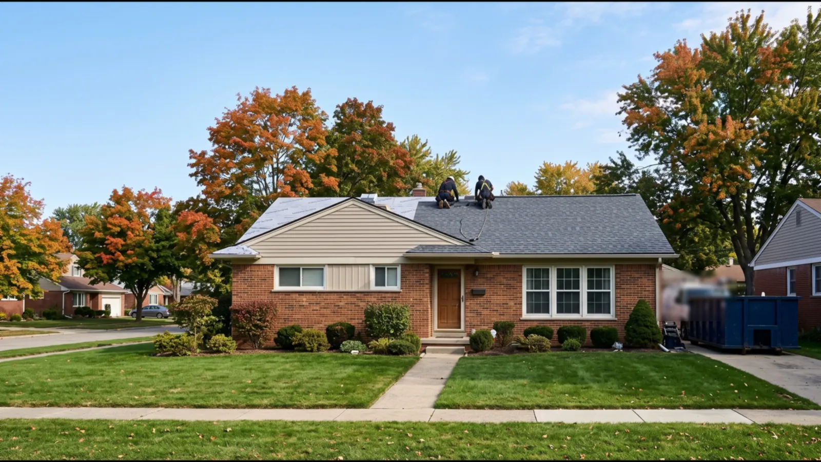 Brick ranch house mid roof replacement, with new charcoal architectural shingles on one side and two roofers in harnesses working near the ridge